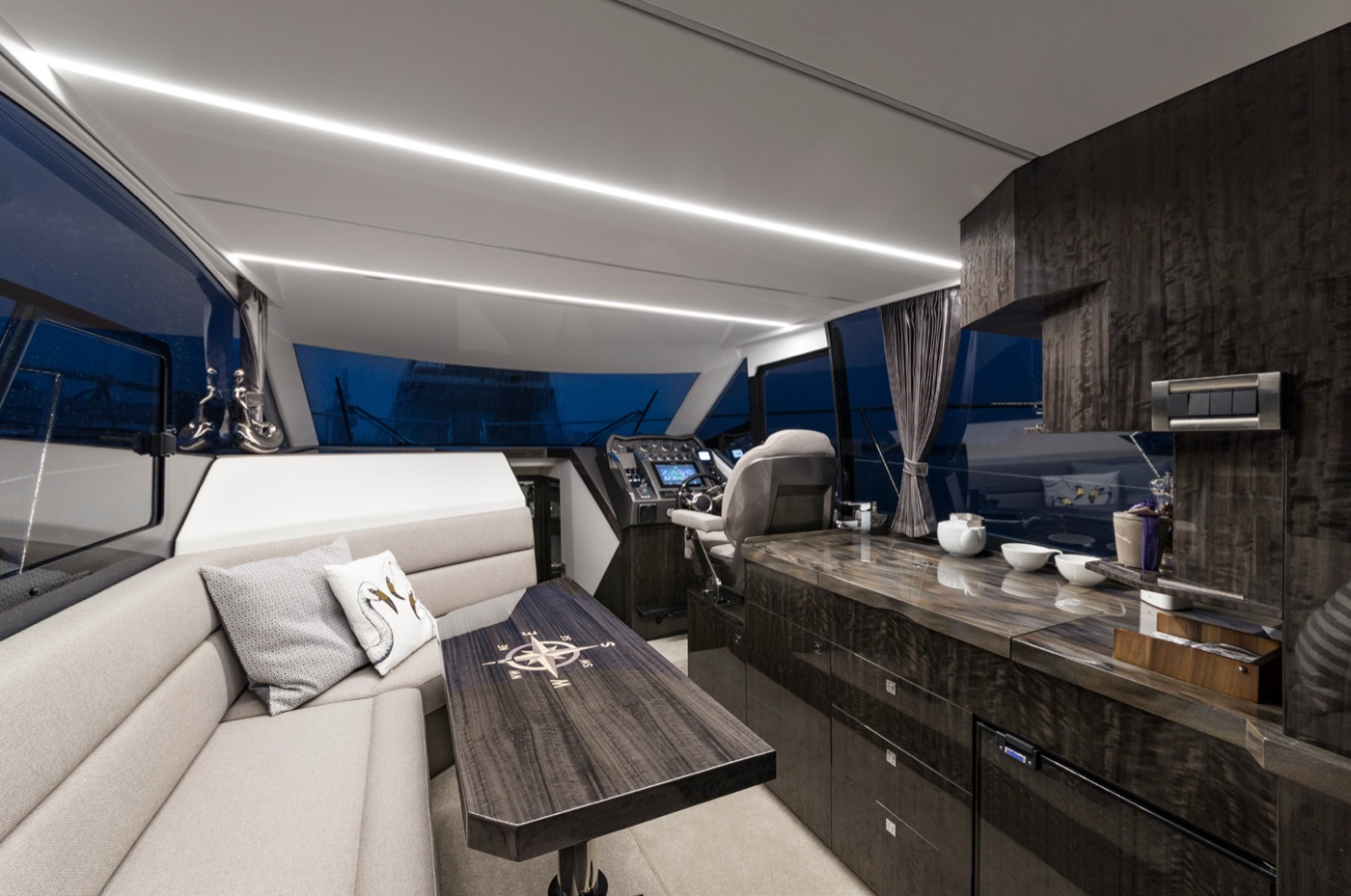 Main deck salon at dusk: L-shaped sofa, dining table, helm and galley counter
